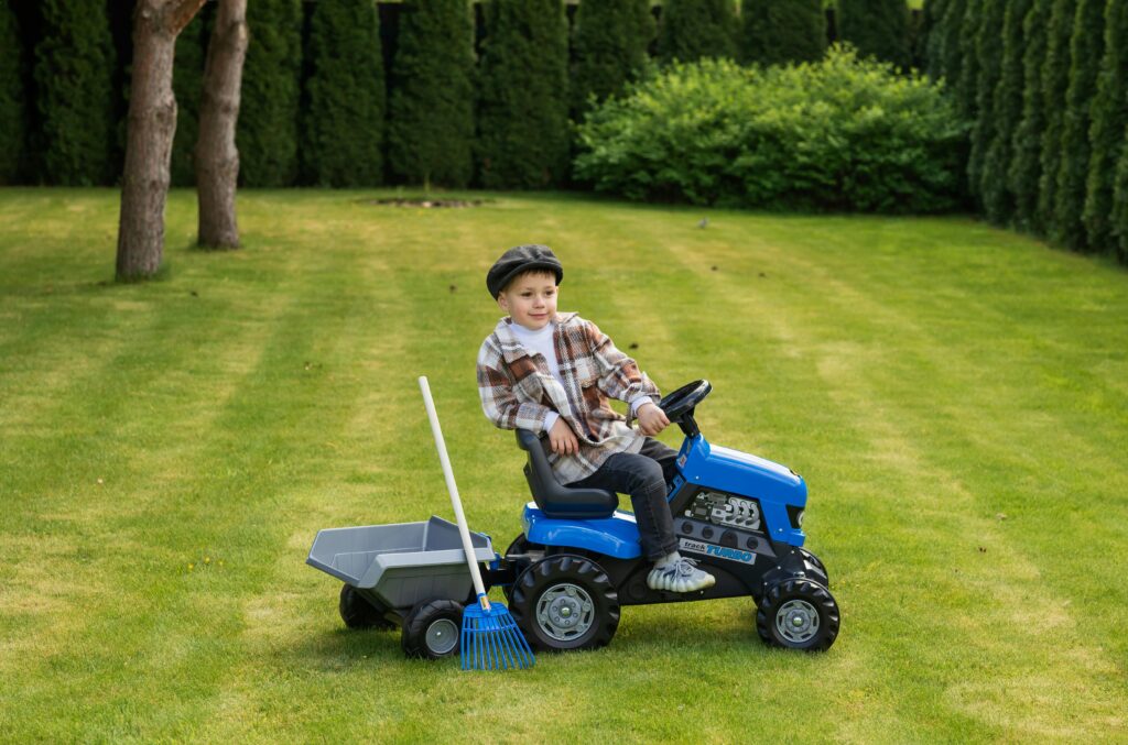 A young boy enjoys a ride on a toy tractor in a lush green garden, capturing playful outdoor fun.